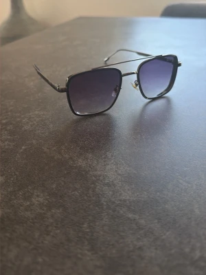 fyrkantiga Gucci solglasögon - Snygga solglasögon med svart metallbåge och fyrkantiga glas. Glasen har en mörk toning som går från svart till lila. Tunn och stilren design med näskuddar för extra komfort. Perfekta för att lyfta din look under soliga dagar.