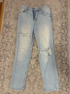 Zara Ljusblå slitna jeans - Säljer ett par ljusblå jeansfrån Zara med raka ben och slitningar vid ena låret och ena knät. Jeansen har klassisk femficksmodell och hög midja. Perfekta för en avslappnad och trendig look. 