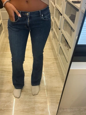 Mörkblå bootcut jeans - Säljer ett par mörkblå bootcut jeans med klassisk femficksdesign och normal midja. Jeansen har en snygg passform som sitter tajt över låren och släpper ut lite vid bensluten. Perfekta till vardagslooken och passar till det mesta.