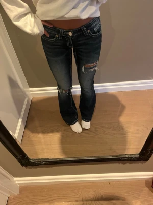 Jeans - Ett par mörkblåa lågmidjade bootcut jeans med slitningar på benen
