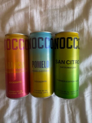 Nocco energidryck 3 smaker - Tre burkar Nocco energidryck i smakerna Arancia (apelsin/granatäpple), Pomelo (citrus) och San Citro (satsuma/lime). Alla är sockerfria och innehåller 180 mg koffein per burk. Färgglada burkar i orange, blå och grön nyans, 330 ml vardera.