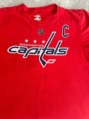 Röd Washington Capitals t-shirt M  - Säljer en röd t-shirt med Washington Capitals tryck framtill och NHL-logga. T-shirten har korta ärmar och rund hals. Perfekt för dig som vill visa vilket lag du hejar på! Materialet är mjukt och skönt bomull.