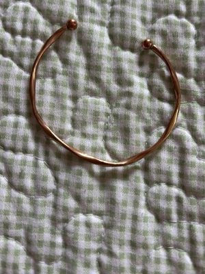 Guldigt öppet armband i metall - Snyggt och minimalistiskt armband i guldfärgad metall. Armbandet är öppet med två små kulor i ändarna och har en lätt tvinnad form som ger en modern touch. Perfekt för dig som gillar stilrena accessoarer med en twist.