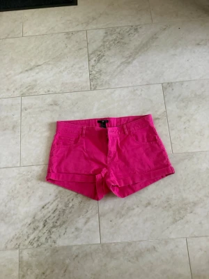 Rosa shorts från H&M - Snygga rosa shorts från H&M i klassisk femficksmodell. De har normal passform och är tillverkade i bomull, perfekta för varma dagar. Stängs med knapp och dragkedja framtill.