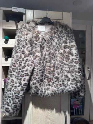 Leopardmönstrad fuskpälsjacka - Säljer en fluffig och trendig leopardmönstrad fuskpälsjacka, Jackan har långa ärmar och en rak passform. Perfekt för dig som vill sticka ut och hålla dig varm under vintern. Färgerna går i beige, brunt och svart för en cool look. Jackan har fickor storlek s men passar en m också