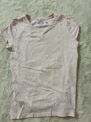 Ljusrosa ralph Lauren t-shirt  - Snygg ljusrosa t shirt från Ralph Lauren. Har en fläck vid kragen men annars i bra skick. Storlek barn L (12-14 år)