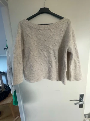 Beige stickad tröja Gina Tricot - Mysig beige stickad tröja från Gina Tricot med kabelstickat mönster. Tröjan har bred ribbad halsringning, långa ärmar och ribbade muddar. Perfekt för kalla dagar och enkel att matcha till olika outfits.