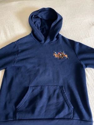 Polo Ralph Lauren Hoodie 158 - 168 cm - Snygg mörkblå hoodie från Polo Ralph Lauren med broderat polospel-motiv på bröstet. Klassisk känguruficka framtill och stor huva. Tillverkad i mjuk bomull som känns skön mot huden. Youth XL (18–20) – motsvarar ungefär vuxen XS/S.