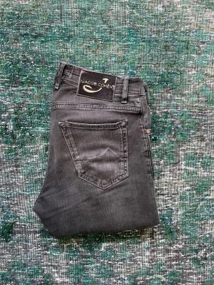 Jacob Cohën Jeans I Limited Edition - Snygga grå jeans från Jacob Cohen, limited edition style 688. Klassisk femficksmodell med knappgylf och diskreta slitningar. Jeansen har en svart patch med logga bak och detaljer i silver. Perfekta för dig som gillar exklusiva och stilrena jeans.