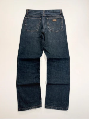 Mörkblå jeans med vintagekänsla - Säljer ett par mörkblå jeans med rak passform och klassiska fem fickor. Jeansen har en vintage vibe med subtila slitningar och kontrastsömmar. Materialet är kraftig denim som ger en tidlös look. Perfekta för dig som gillar en avslappnad och stilren stil.