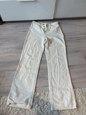 Vida vita jeans med raka ben - Säljer ett par vita jeans med raka ben och hög midja. Jeansen har knappgylf och klassiska fickor fram och bak. Materialet är denim i bomull och passformen är avslappnad och trendig.