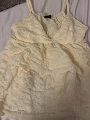 Ljus gult  linne med volanger - Söt ljus gult linne med tunna axelband och volangdetaljer. Linnet  har en omlottliknande överdel och ett skirt, strukturerat tyg som ger en romantisk känsla. Perfekt för varma dagar och sommarens alla tillfällen. Köpt på Gina tricot 