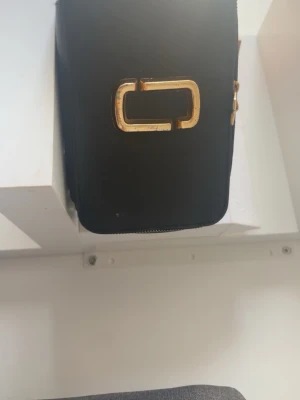 Svart handväska med gulddetaljer/ marc jacobs  - Snygg marc jacobs väska. Den fungerar jätte bra men har dock inte band! knappast använd ! pris kan diskuterad
