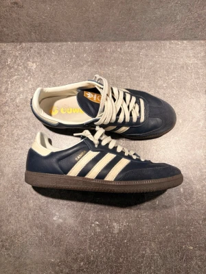 Adidas Samba mörkblå sneakers - Säljer ett par riktigt fina Adidas Samba i mörkblått/navy med cremefärgade detaljer och brun gum-sula.  👟 Storlek: 42 2/3 ✨ Skick: Nyskick – endast använda 3–4 gånger 💰 Nypris: ca 1 500–1 600 kr 📦 Skorna är väl omhändertagna och har inga större tecken på användning.