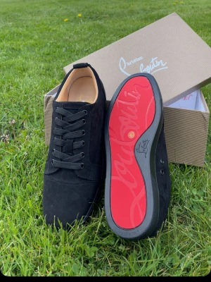 Christian Louboutin - Snygga svarta sneakers från Christian Louboutin som knappt använda. väldigt fint skick och  i mocka med klassisk röd sula och svarta skosnören. Låg modell med stilren design och exklusiv känsla. Perfekta för dig som vill sticka ut med en ikonisk detalj på fötterna. 