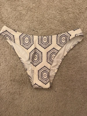 Vit bikiniunderdel med grafiskt mönster - Snygg bikiniunderdel i vitt med svart grafiskt mönster. Klassisk modell med medelhög midja och bekväm passform. Perfekt för stranddagar eller poolhäng.