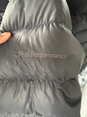 Svart dunjacka från Peak Performance - Snygg svart dunjacka från Peak Performance med diskret logga broderad på bröstet. Jackan har hög krage och dragkedja framtill. Fick köpa den av min syssling som kanppt använt den när den va ny sen så anvönde jag den i ca 2-3 mån. Den är herr storlek M. Vääääldigt fint skick där av priset. Skulle säga nyskick men den har inga lappar kvar så kan inte klicka i det.