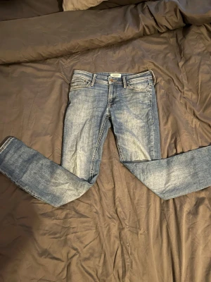 Blå jack & Jones jeans - Säljer ett par jack & Jones jeans med tvättad look och raka ben. Jeansen har fem fickor, bälteshällor och stängs med knapp och dragkedja. Perfekta för en avslappnad och trendig stil.