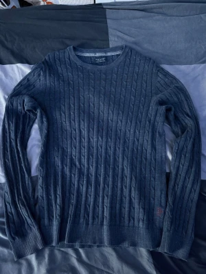 Mörkblå kabelstickad tröja Jack & Jones - Mörkblå kabelstickad tröja från Jack & Jones Premium med rund halsringning och ribbade muddar. Tröjan har ett klassiskt mönster och är perfekt för lager-på-lager. Materialet är mjukt och bekvämt.