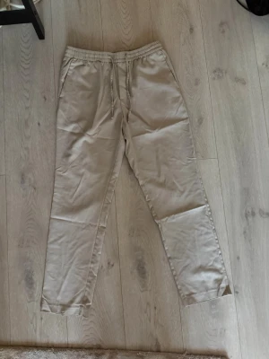 Beige mjukisbyxor/chinos - Säljer ett par beige mjukisbyxor med resår i midjan och dragsko för skön passform. Byxorna har raka ben och sidofickor. Perfekta för chill dagar eller när du vill ha det extra bekvämt. Extremt bekväma 