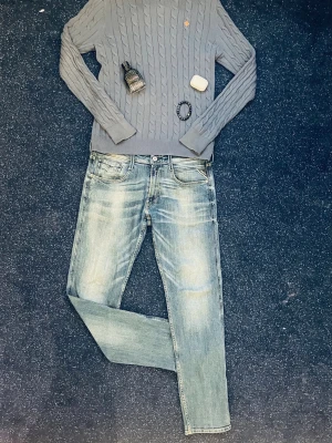Grå kabelstickad tröja Morris tröja - Snygg marinblå kabelstickad tröja med rund hals och långa ärmar. Tröjan har ribbade muddar vid ärmslut och nederkant samt ett diskret broderat emblem på bröstet. Perfekt för dig som gillar klassisk och stilren design.