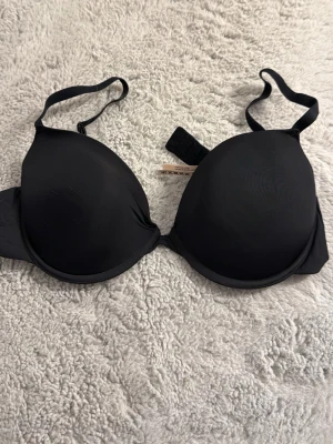 Svart push-up bh från Kappahl - Stilren svart push-up bh från Kappahl med släta kupor och justerbara axelband. Bh:n har bygel och vaddering för extra stöd och form. Tillverkad i mjukt, stretchigt material som känns bekvämt mot huden.