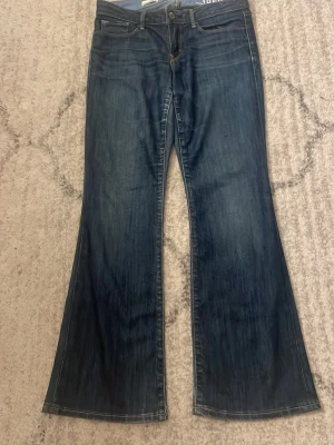 Mörkblå bootcut jeans - Snygga mörkblå bootcut jeans med klassisk femficksmodell och lätt slitna detaljer. Jeansen har hög midja och vida ben som ger en retrovibe. Tillverkade i denim med en skön känsla och passar perfekt till sneakers eller boots.