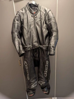 Svart skinnställ från Alpinestars - Säljer ett svart skinnställ från Alpinestars i storlek 50 Passar tyvärr inte mig då jag är 176cm skulle passa runt 170 perfekt!. Stället är tillverkat i 100% Läder med foder i polyester. Det har dragkedja framtill, vadderade partier och tydliga Alpinestars-loggor på ben och bröst. Perfekt för dig som kör motorcykel och vill ha grym stil.