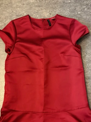 Röd kort klänning från Divided - Snygg röd klänning från Divided H&M med rund halsringning och korta ärmar. Klänningen är enkel och stilren, perfekt för dig som gillar minimalistisk design. Tillverkad i ett mjukt polyestertyg som känns skönt mot huden.