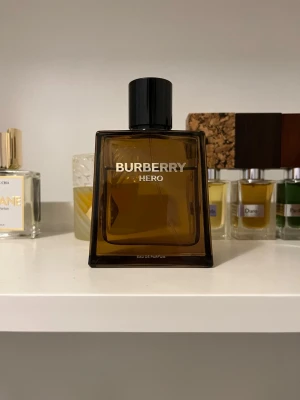 Burberry Hero Eau de Parfum 100 ml - Burberry Hero Eau de Parfum i en stilren, fyrkantig flaska i brunt glas med svart kork. Doften kommer i en matchande brun kartong och flaskan rymmer 100 ml. Perfekt för dig som gillar eleganta och moderna parfymer med exklusiv känsla.
