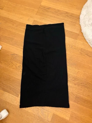 Svart  långkjol - En svart långkjol med rak passform och ribbad struktur. Kjolen är enkel och stilren, perfekt att matcha med olika toppar. Materialet är mjukt och stretchigt, vilket ger en bekväm känsla.