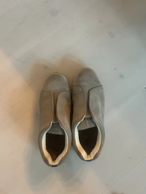 Eytys skor  - Snygga beige/grå slip-on sneakers i mocka med minimalistisk design och rundad tå. Skorna har en ljus sula och insida i vitt tyg. Perfekta för dig som gillar stilrena och enkla sneakers till vardagslooken.