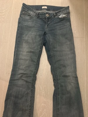 Blå bootcut jeans med mellan blå tvätt - Säljer ett par blå bootcut jeans med snygga slitningar och klassisk femficksmodell. Jeansen har en något utsvängd passform nedtill. Tillverkade i denim med en tvättad look.