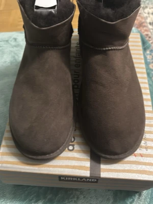 Bruna fårskinnsstövletter Kirkland - Mysiga bruna stövletter från Kirkland i storlek 38. Tillverkade i mjukt mockaliknande material med varmt fårskinnsfoder. Klassisk rund tå och enkel design som passar till många olika stilar. Perfekta för kalla dagar.