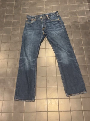 Selvedge Levis 501 30/30 - Säljer ett par blå levis jeans med rak passform och fem fickor. Jeansen har klassiska kontrastsömmar och knappgylf. Materialet är denim i 100% bomull. Perfekta för en avslappnad och tidlös stil. De har en unik tvätt och säljs inte längre, liten defekt på framfickorna