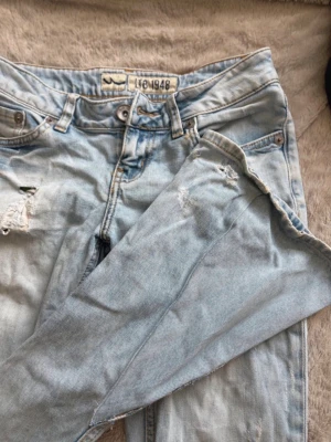 Ljusblå slitna lågmidjade jeans från LTB - Säljer ett par ljusblå jeans från LTB med slitningar och hål för en trendig, avslappnad look. Klassisk femficksmodell med knappgylf och raka ben. Perfekta för dig som gillar en casual streetstyle. 38cm midjemått tvärs över och 82cm innerbenslängd längst sömmen. Pris kan diskuteras! 