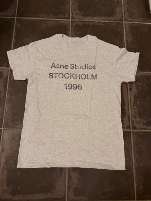 Grå Acne Studios t-shirt Stockholm - Snygg ljusgrå t-shirt från Acne Studios. Perfekt till jeans eller shorts för en clean och enkel look.  Är ca 182 och vägar 66