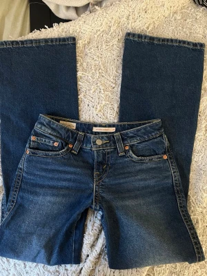 Blå bootcut jeans från Levis med raka ben - Säljer ett par klassiska blå bootcut jeans med raka ben och fem fickor. Jeansen har en snygg tvätt och kontrastsömmar, samt detaljer i kopparfärg vid fickorna. Perfekta för en avslappnad och trendig look.