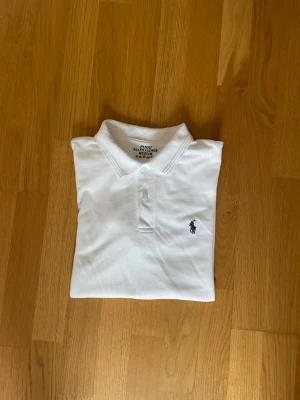 Vit pikétröja från Ralph Lauren - Klassisk vit pikétröja från Ralph Lauren med krage och två knappar framtill. Skicket är mycket bra. Den är köpt begagnad på plick för ett år sedan. Nypris:1695kr