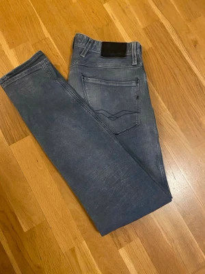 Grå replay  - Snygga grå slim fit jeans från replay med klassisk femficksdesign och diskreta slitningar. Jeansen har en svart patch bak i midjan och raka ben. Perfekta för dig som gillar en enkel men stilren look.