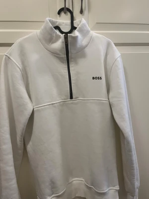 Vit halfzip hoodie från BOSS - Snygg vit hoodie från BOSS med halv dragkedja och hög krage.