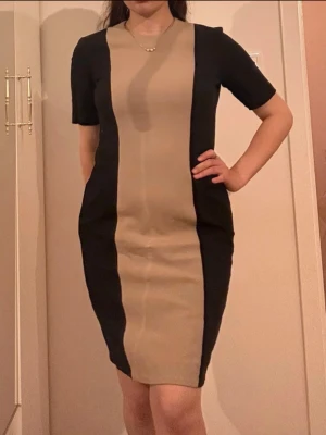 Beige och svart klänning med dragkedja - Elegant och stilig klänning som ger illusionen av en ⏳-kropp. Passar till både formella och fest sammanhang. Passar storlek S-M