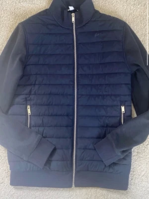 Mörkblå quiltad jacka från Reiss - Snygg mörkblå quiltad jacka från Reiss i storlek XS. Jackan har dragkedja framtill, två fickor med dragkedja och ribbade muddar. Materialet är en mix av vadderad front och mjuka ärmar, perfekt för lager på lager.