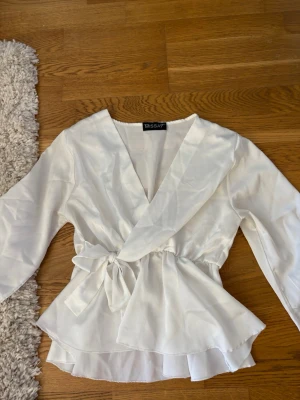 Vit omlottblus från Missay - Snygg vit omlottblus från Missay i ett lätt och flowy material. Blusen har knytband i midjan, v-ringning och volangkant nedtill. Perfekt för dig som gillar en feminin och chic stil. Dock ett märke som inte syns så tydlig av bläck