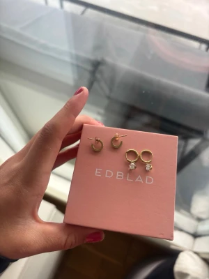 Guldiga örhängen från Edblad - Två par guldiga örhängen från Edblad. Ena paret är små hoops i enkel design, det andra paret är runda hoops med gnistrande stenar som detalj. Perfekta för att mixa och matcha till olika looks. Säljes i originalförpackning. Säljer båda tillsammans för 499kr eller var för sig 250kr