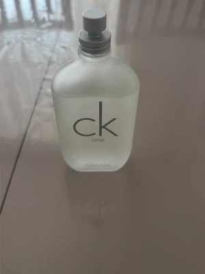 CK One parfym från Calvin Klein - Minimalistisk och stilren parfymflaska i frostat glas med grå spraykork. Flaskan har den ikoniska 'ck one'-loggan tryckt framtill och rymmer en fräsch unisexdoft. Perfekt för dig som gillar klassiska och tidlösa parfymer.