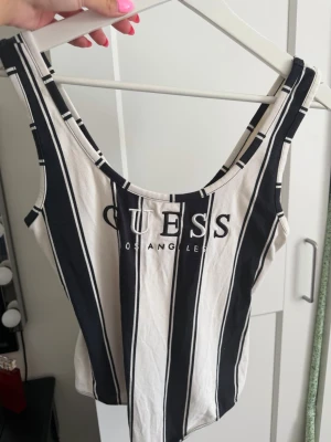 Randig body från Guess - Snygg randig body från Guess med svartvita breda ränder och broderad logga framtill. Modellen är ärmlös med djup urringning och tillverkad i mjukt bomullsmaterial.💕