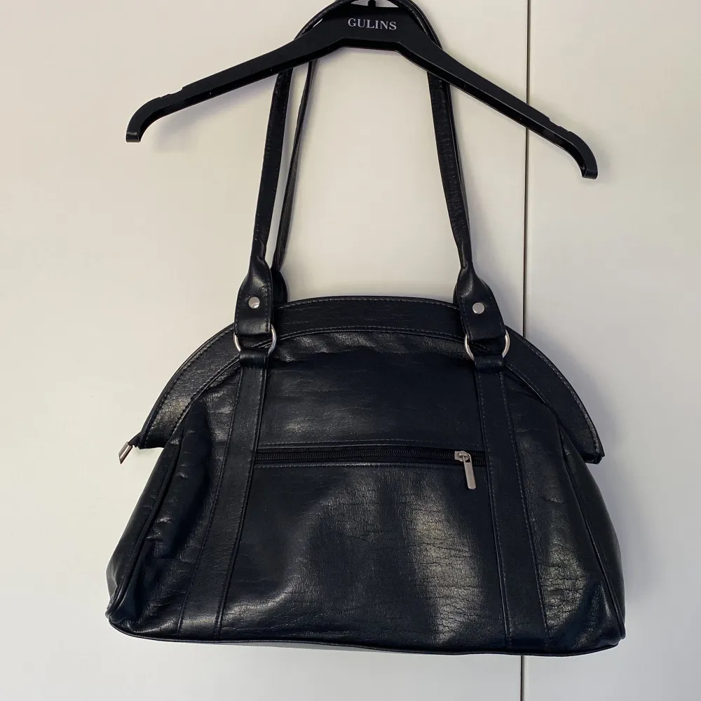 En rymlig svart handväska i läder med silverdetaljer. Har ett fack inuti och stänga med dragkedja! Perfekt för en liten dator eller anteckningsböcker till skolan🖤🖤🖤. Väskor.