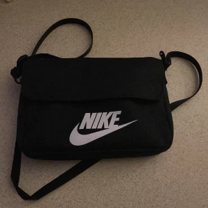 Nike Axelväska  - Svart Nike Axelväska  Stängs med knappar  4st fickor 2 st fickor med dragkedja Är i bra skick  