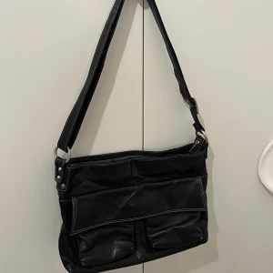 Svart väska  - Super snygg skinn väska köpt second hand.  Har själv använt som väska till skola då den rymmer dator och böcker, den är även justerbar.  Mått: 33x20 cm 